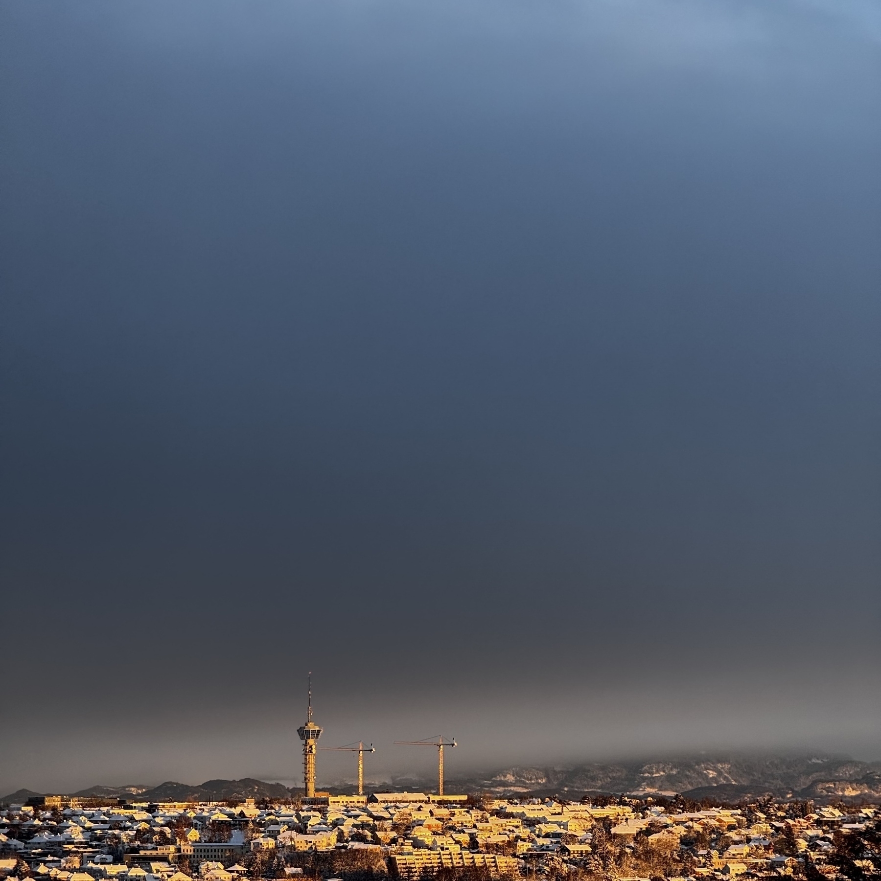 A cityscape under a dark, cloudy sky features a distinct tower and a wide horizon.